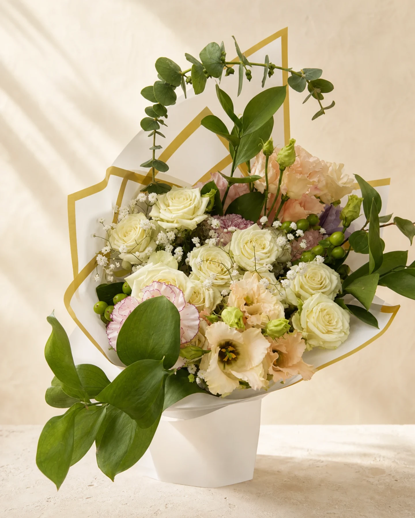 Ivory rose and blush flower bouquet with eucalyptus and gold-edged white wrapping